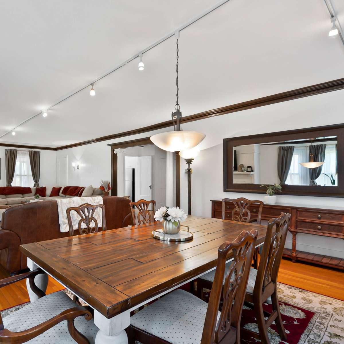 A spacious living and dining area features a wooden dining table surrounded by upholstered chairs, with a sectional sofa and a fireplace in the background.
