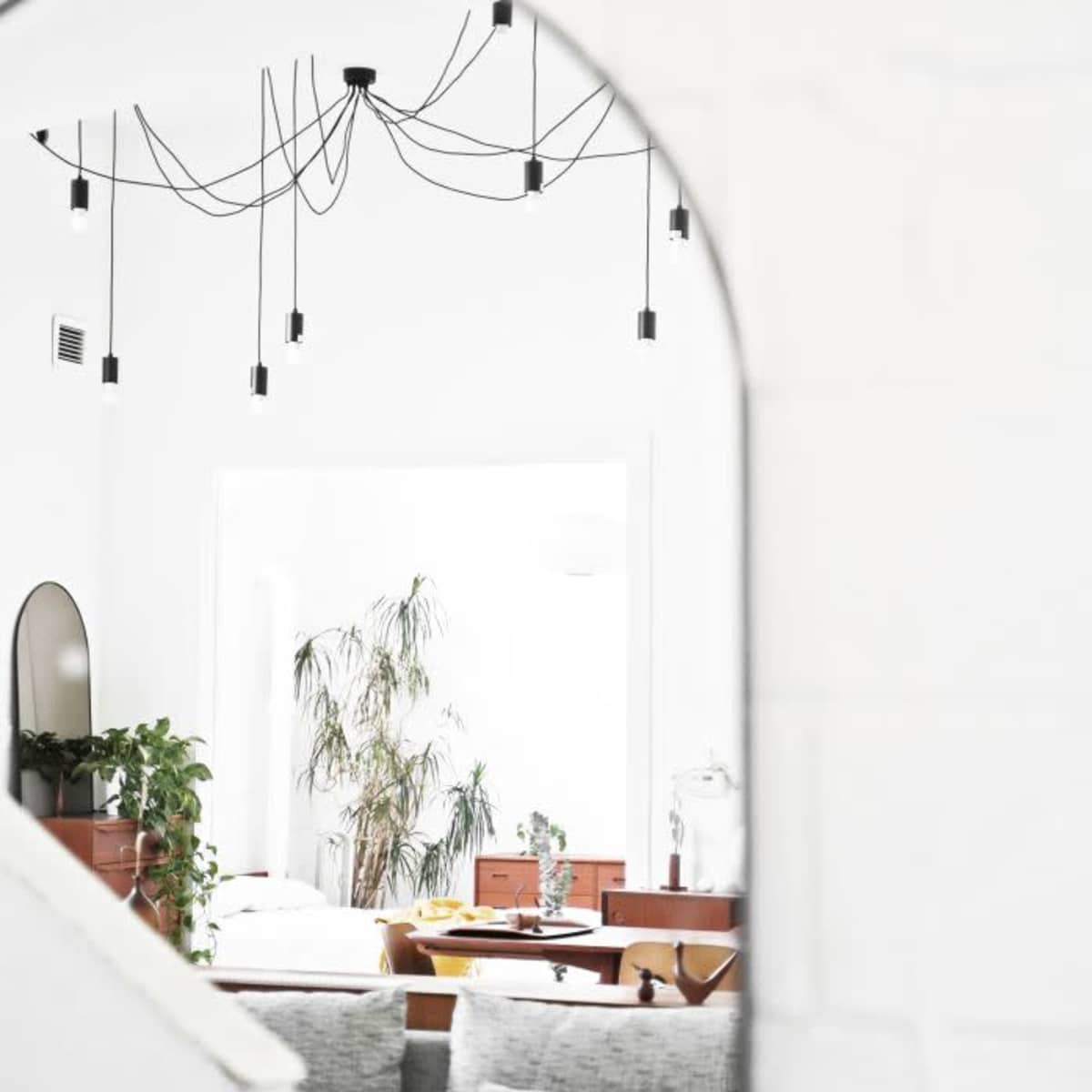 A view through an archway reveals a bright room with hanging light fixtures, plants, and minimalistic furniture.
