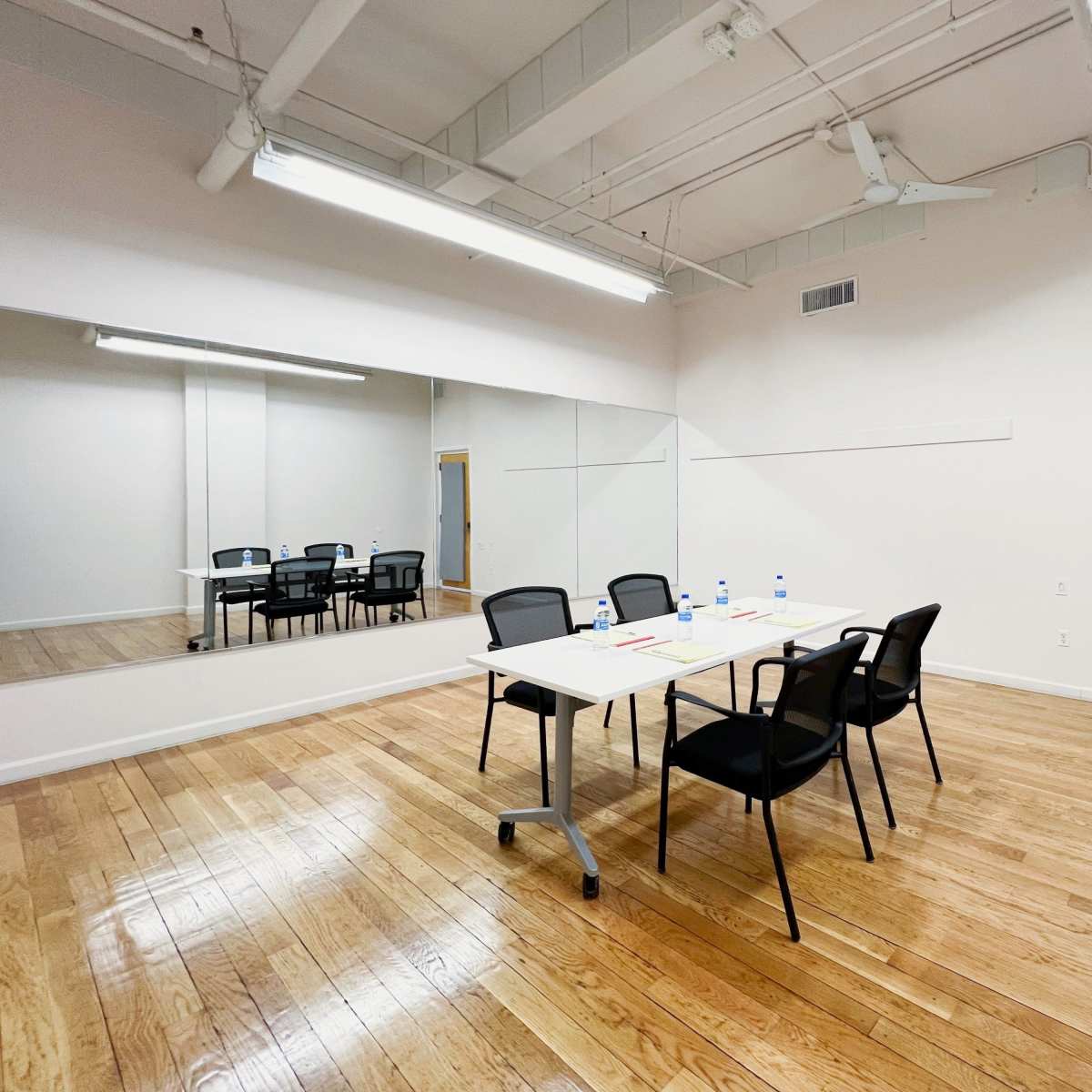 A conference room is shown with a table and chairs set up, and a large mirror on one wall.