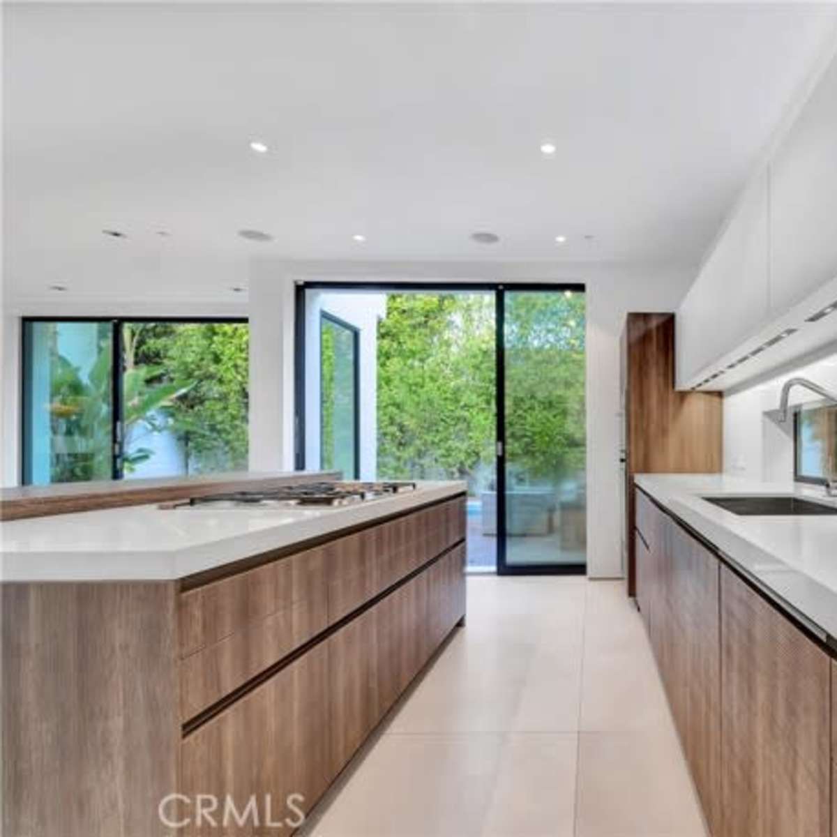 A modern kitchen with wooden cabinetry, a large island, and sliding glass doors that open to an outdoor area.