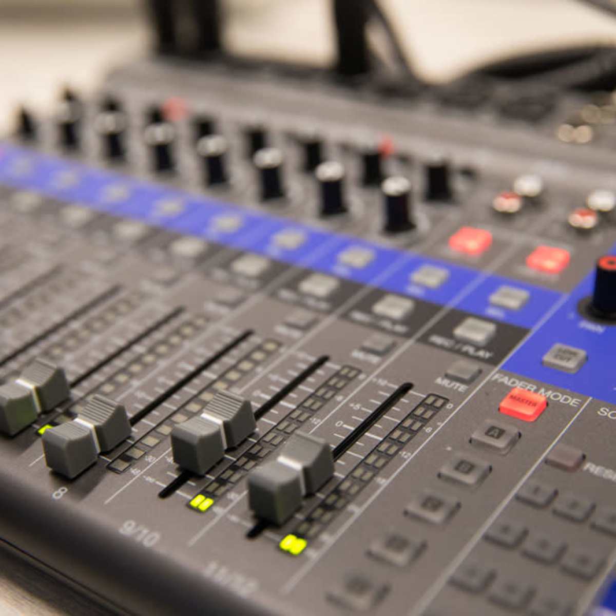 A close-up of an audio mixing console with various sliders, buttons, and knobs arranged in a grid layout.