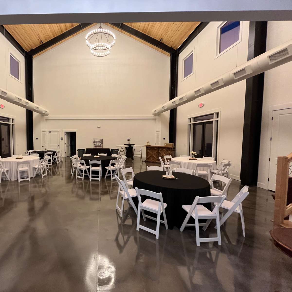 A spacious indoor event hall with round tables dressed in black and white linens, illuminated by a large chandelier.