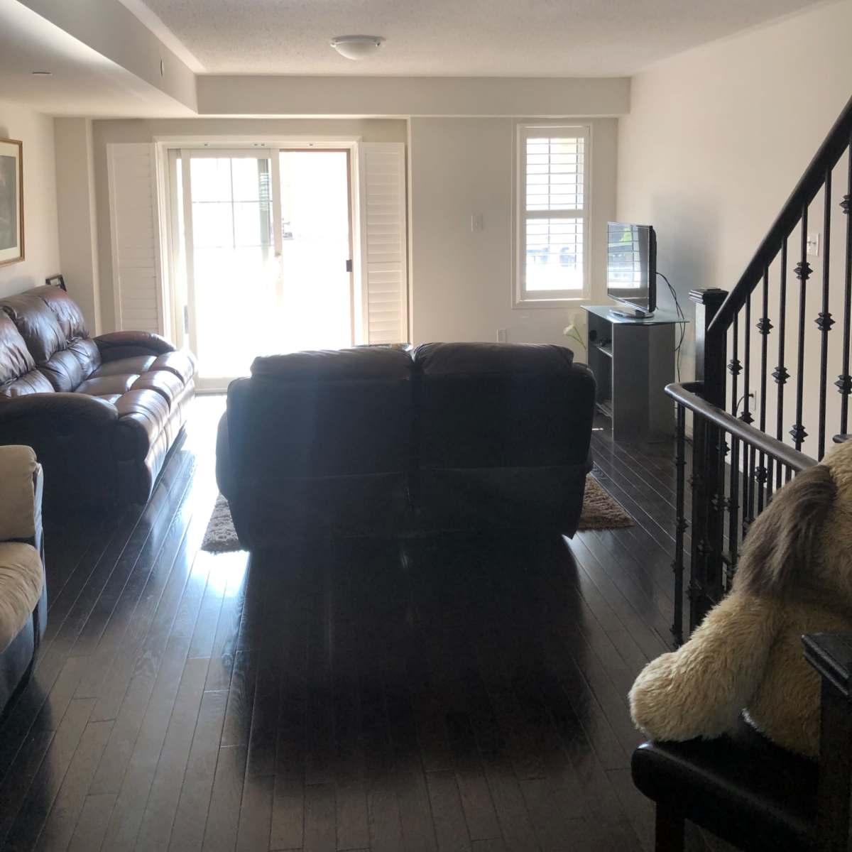 The room features a living area with two sofas, a television, and access to a balcony through sliding glass doors.