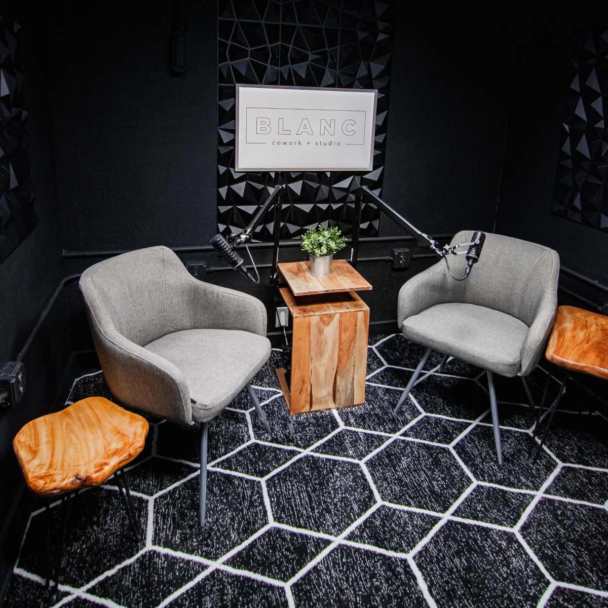 A small recording studio with two gray chairs, a wooden table with a plant, and two overhead lights.