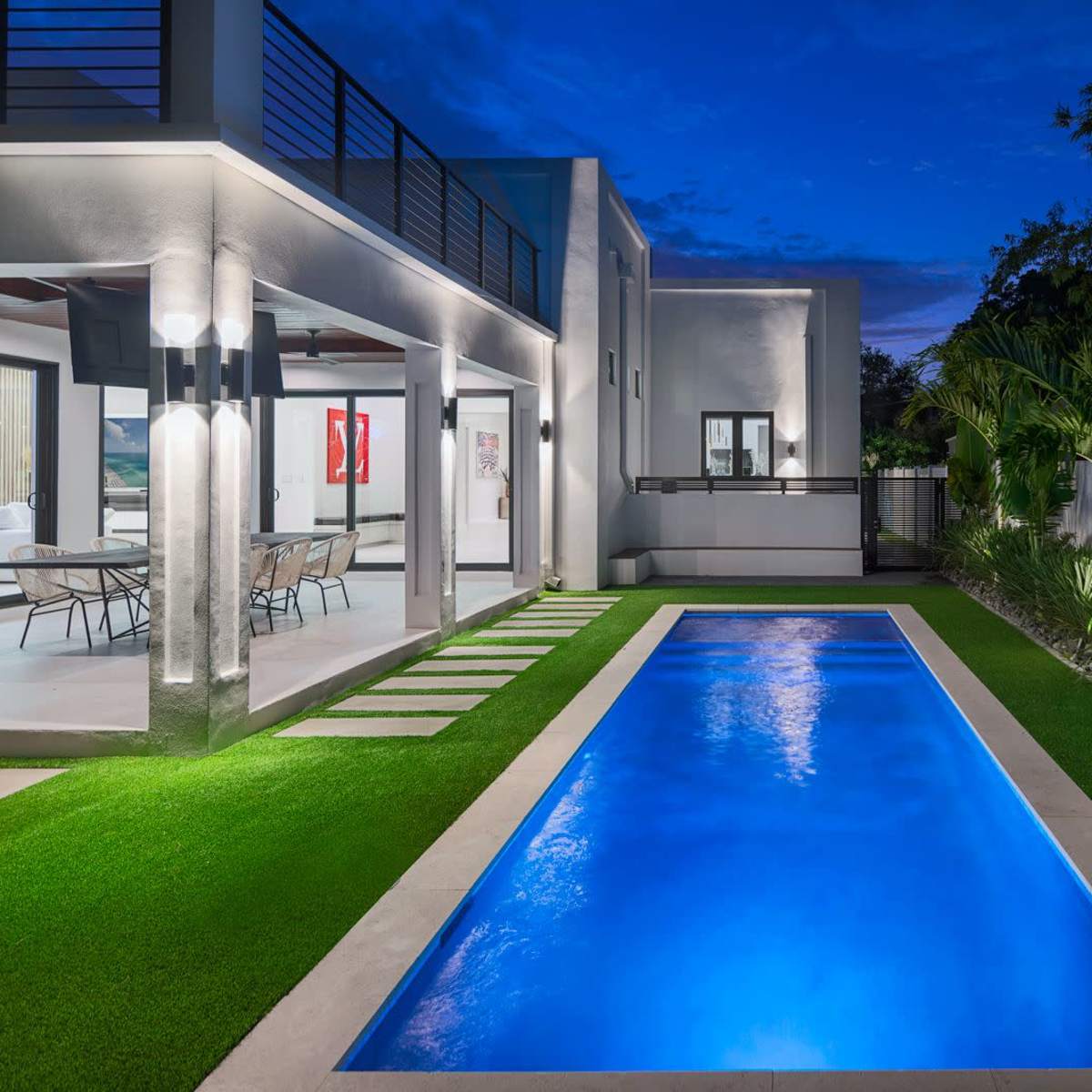 A modern home features a sleek swimming pool surrounded by landscaped greenery and stone pavers under a twilight sky.
