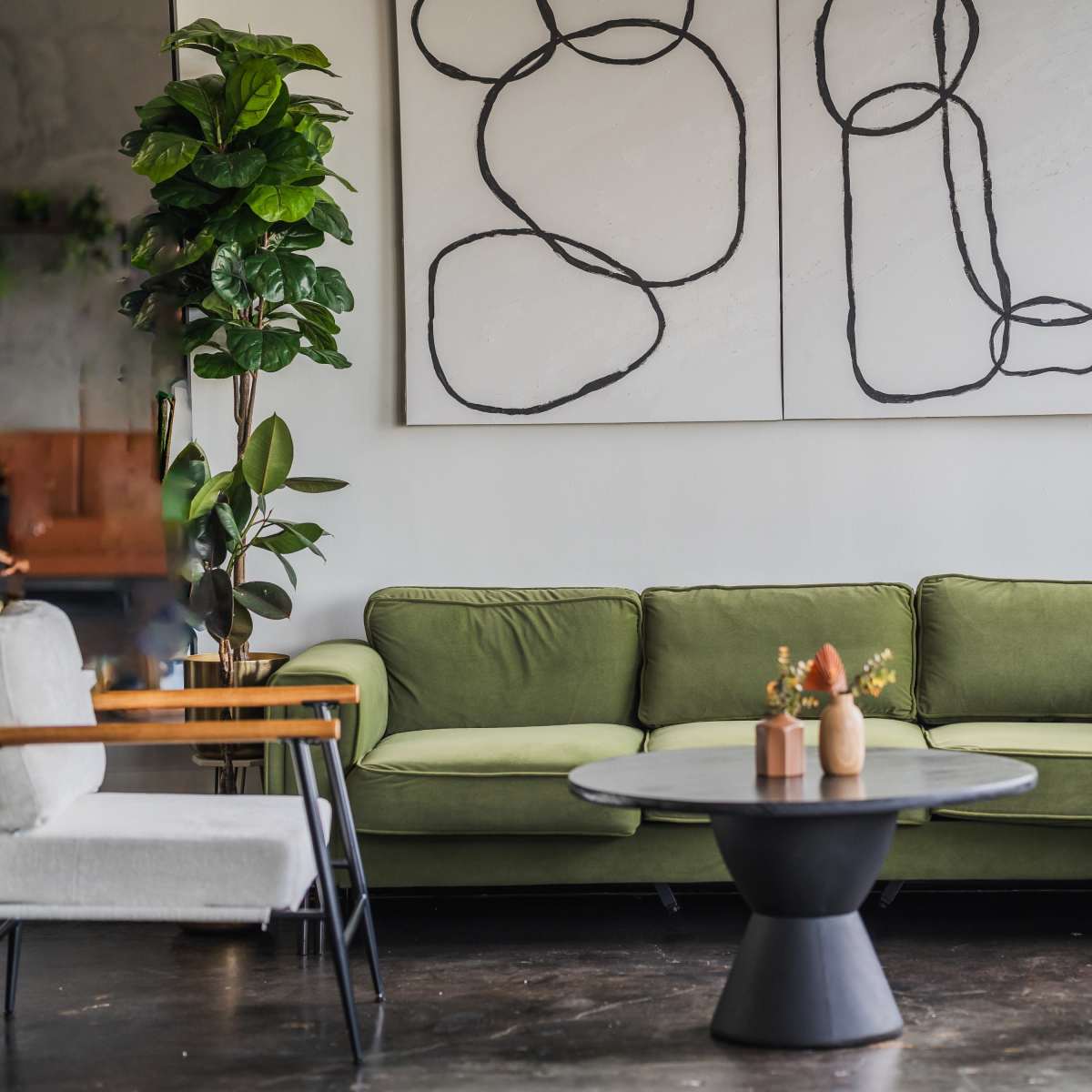 A green couch is positioned in a modern interior, accompanied by a round black coffee table and abstract art on the walls.