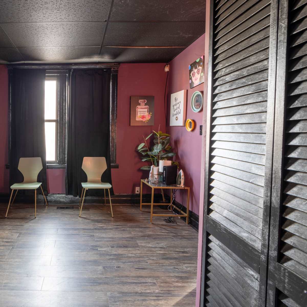 A small, purple-walled room with two chairs and an armchair facing a window, illuminated by natural light.