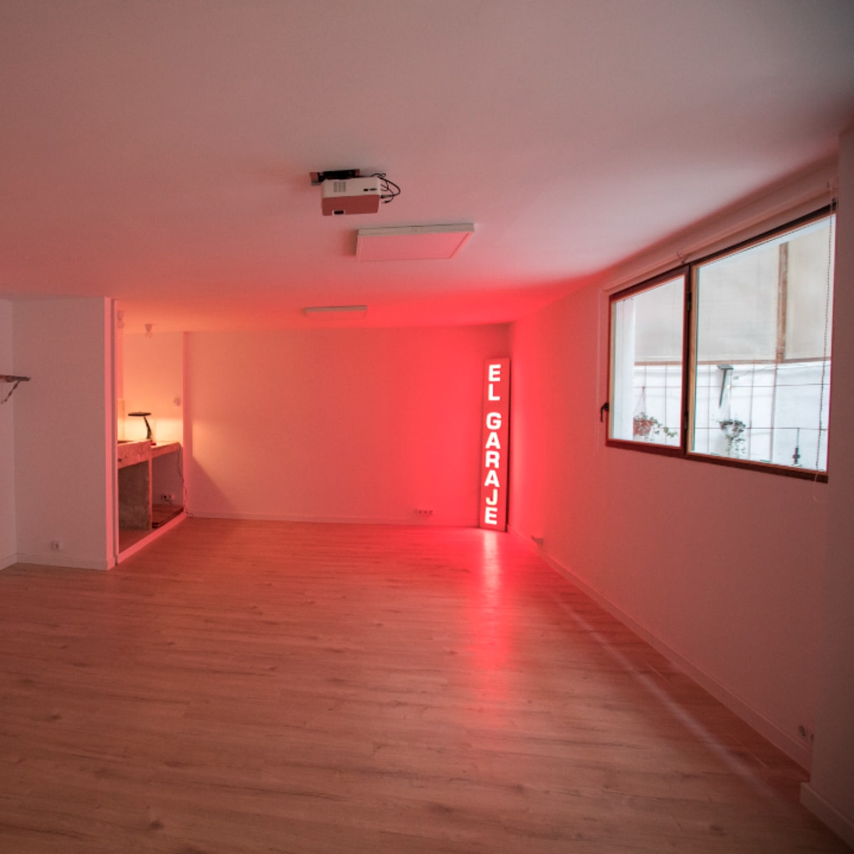 A spacious, empty room featuring wooden flooring, a guitar on the wall, a bar area, and a neon sign that says "EL GARAJE."
