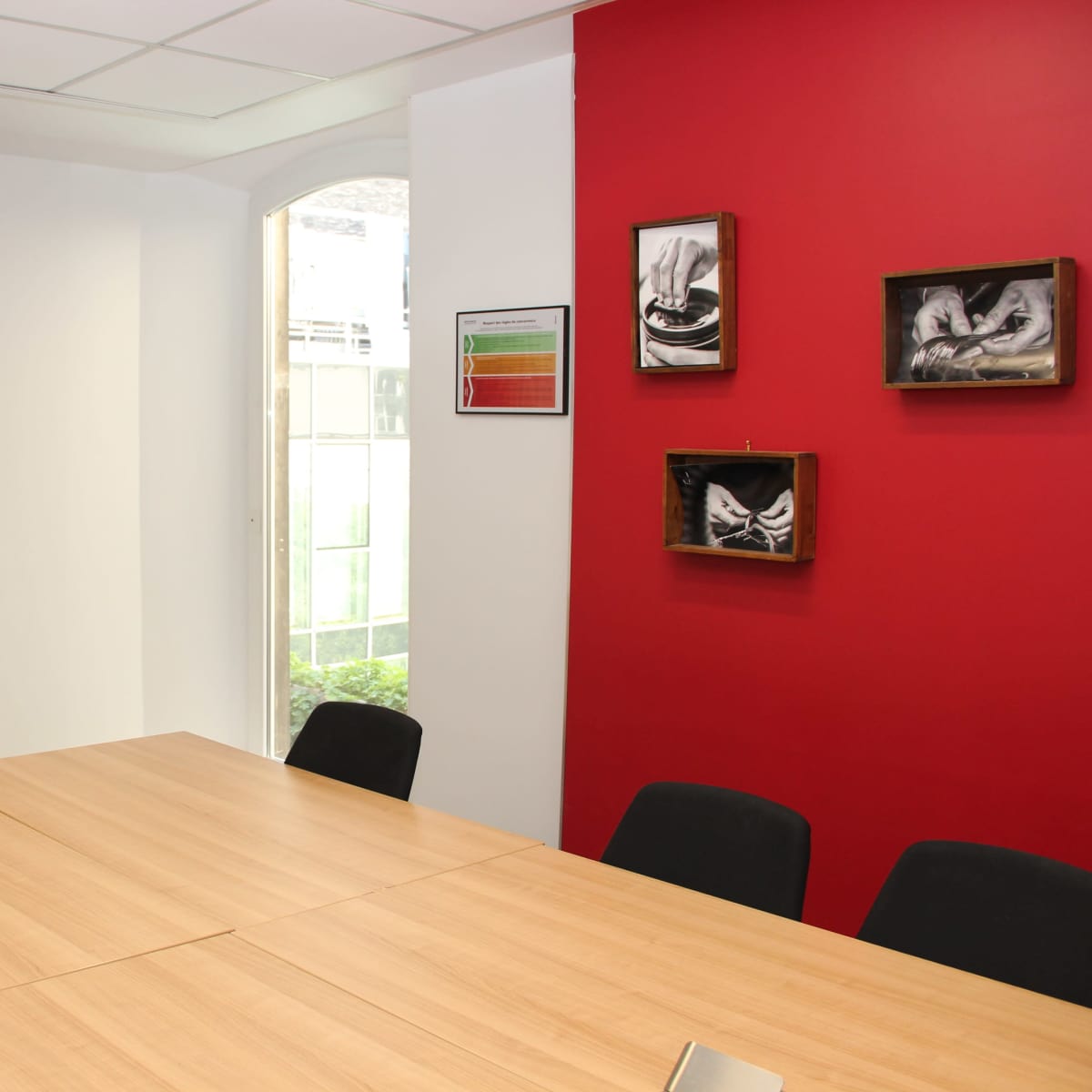 A conference room featuring a large table, black chairs, a wall-mounted television, and framed artwork on a red wall.