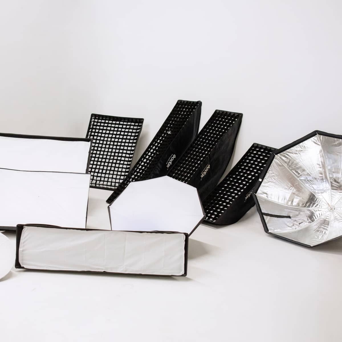 Various photography lighting modifiers arranged on a neutral background.
