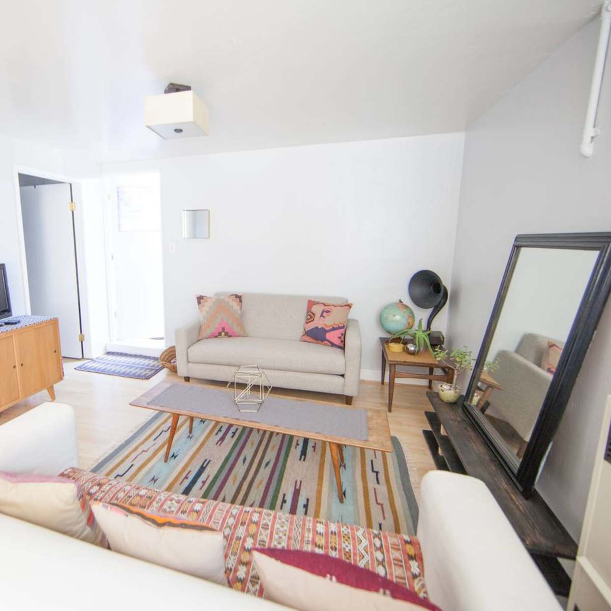 A modern living room features a beige sofa, a wooden coffee table on a patterned rug, a small television, and a door leading outside.