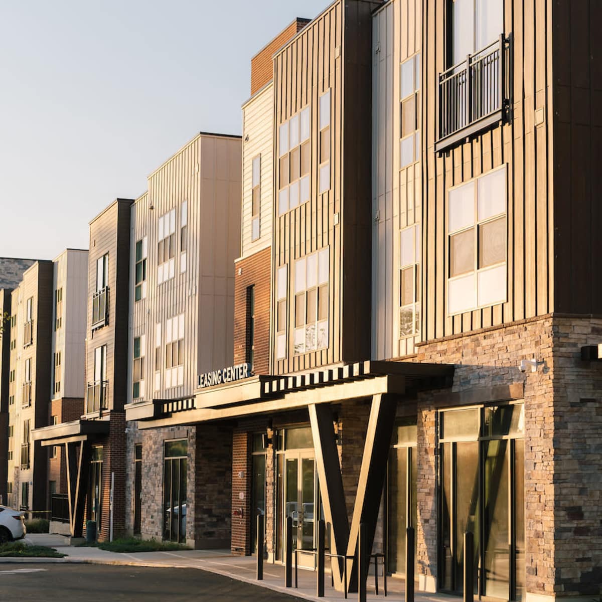 A modern multi-story apartment building with a leasing office, featuring a combination of wood and stone exteriors.