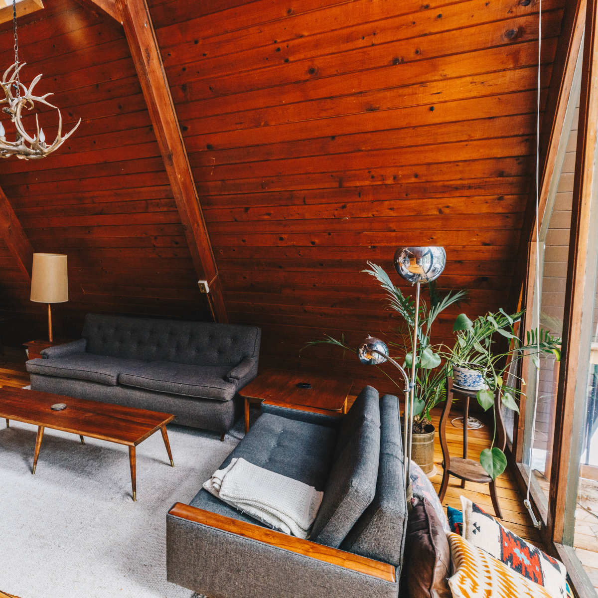 A wooden A-frame living room with a brown paneled ceiling, two couches, a coffee table, and a large window letting in natural light.