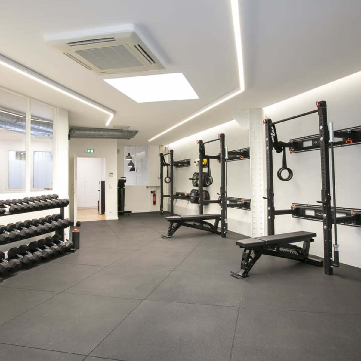 A well-organized gym interior featuring a rack of dumbbells, a weight bench, and wall-mounted strength training equipment in a spacious layout.