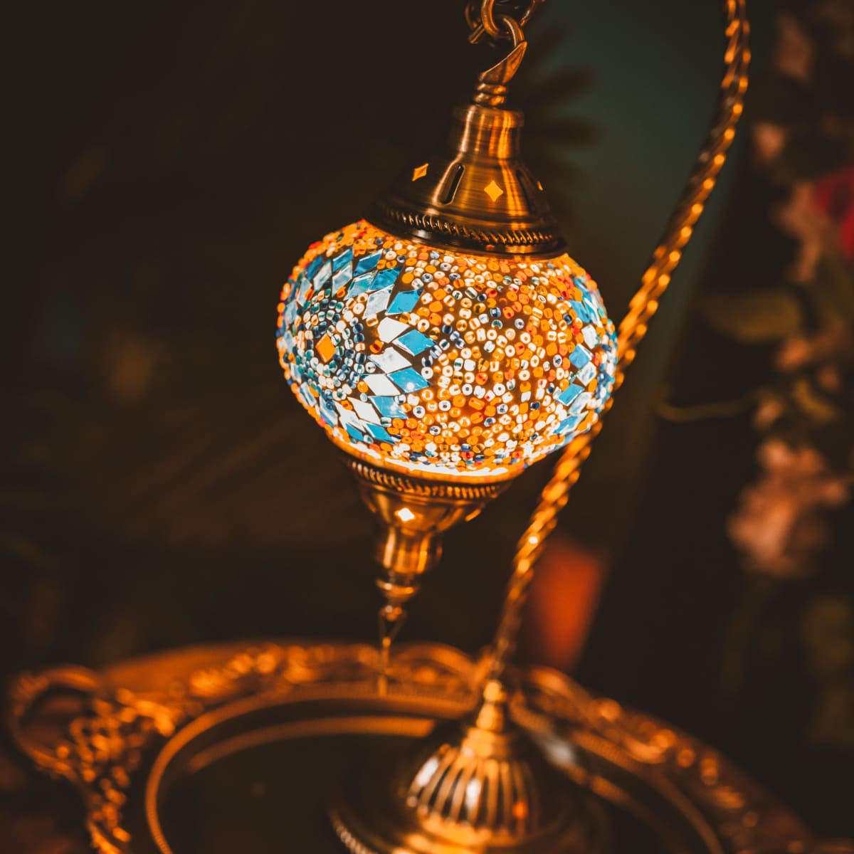 A decorative lamp with a colorful mosaic design sits atop a polished wooden table next to a mirrored tray.
