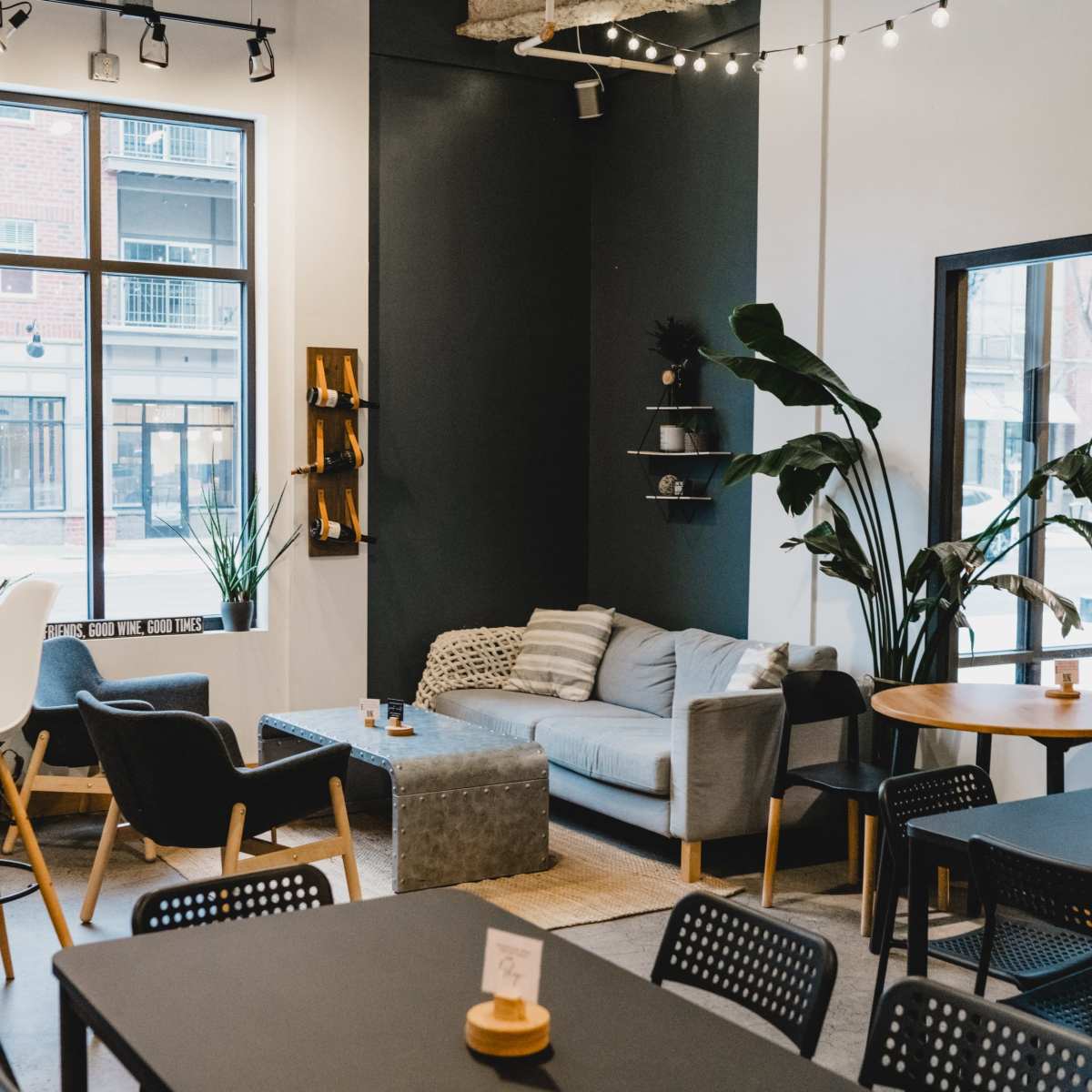 A modern café interior with tables, plants, and a seating area featuring a gray sofa.