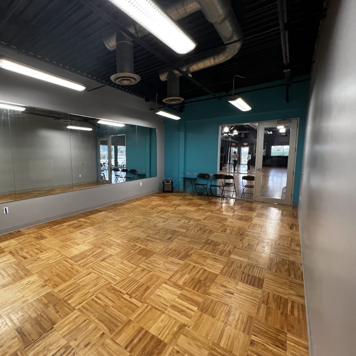 A spacious room with a wooden floor, mirrors on one wall, and teal-colored accent walls.
