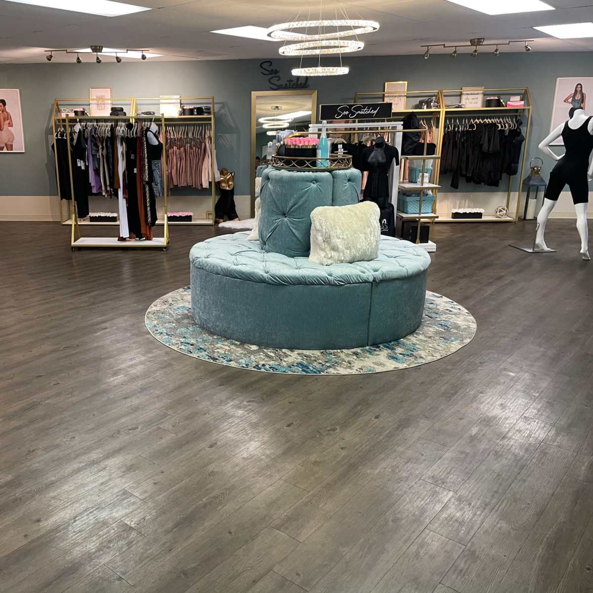 A spacious boutique with racks of clothing and a central circular seating area, featuring soft lighting and elegant decor.