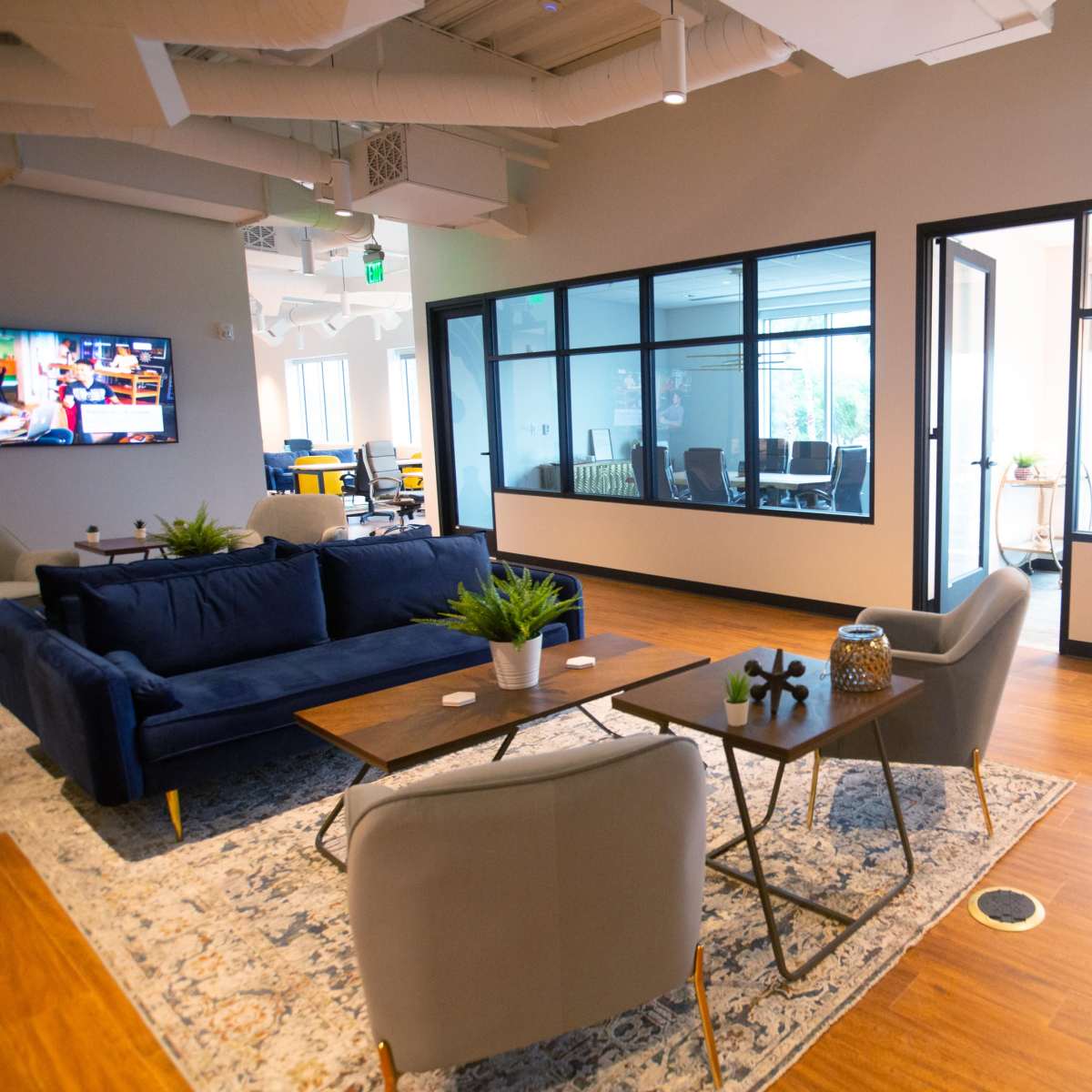 A modern office space featuring a sitting area with a navy sofa, a coffee table, and a view of glass-walled meeting rooms.