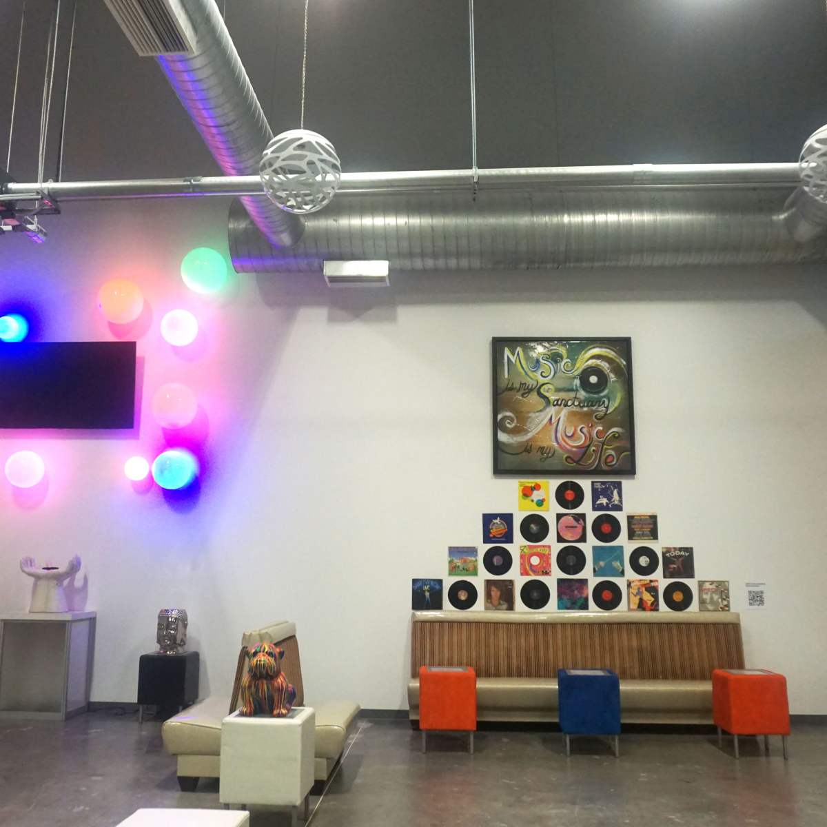 A spacious room features a large wall display of colorful lights and vinyl records, with modern furniture arranged around a central seating area.