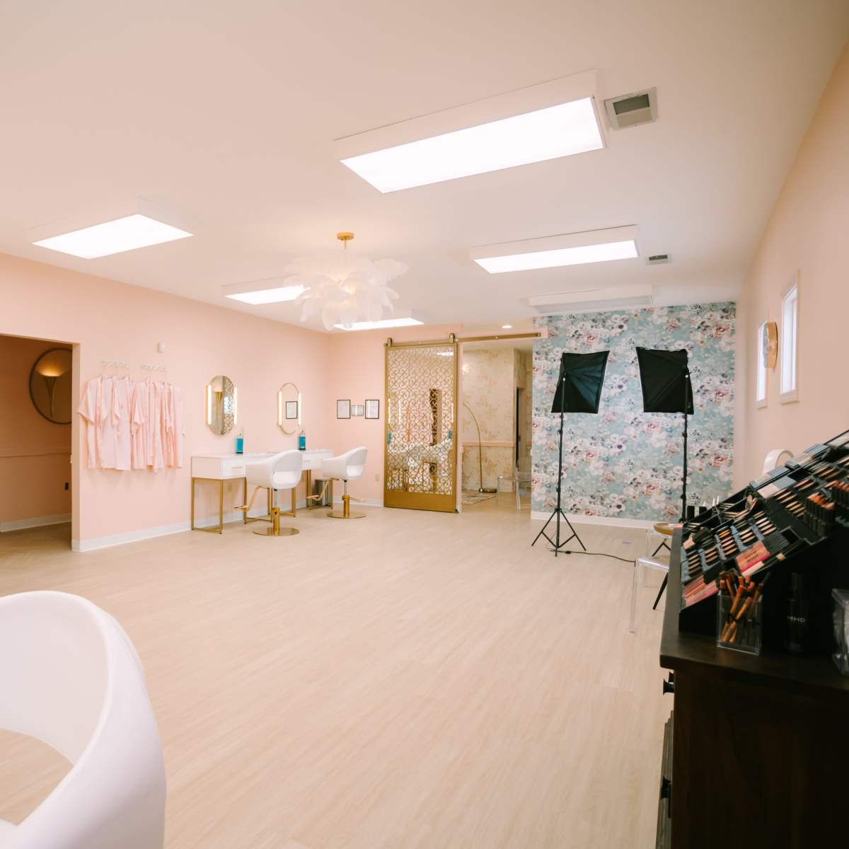 A modern beauty salon with light pink walls, white furniture, and a decorative floral wallpaper in one area.