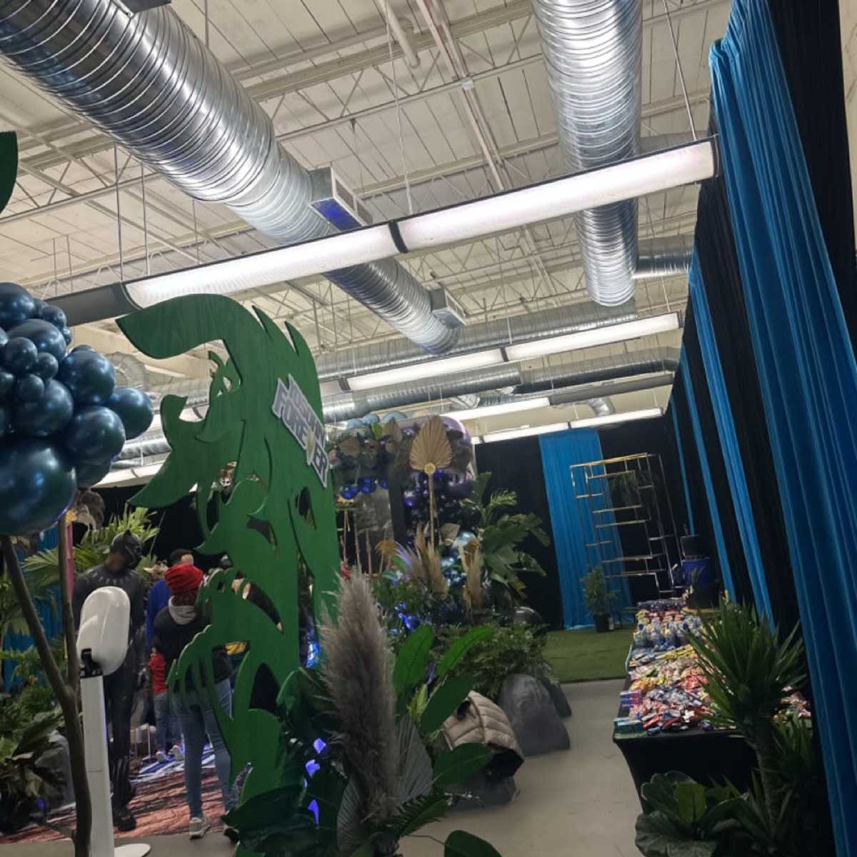 An indoor event space decorated with blue curtains, indoor plants, and shiny metallic vents overhead.