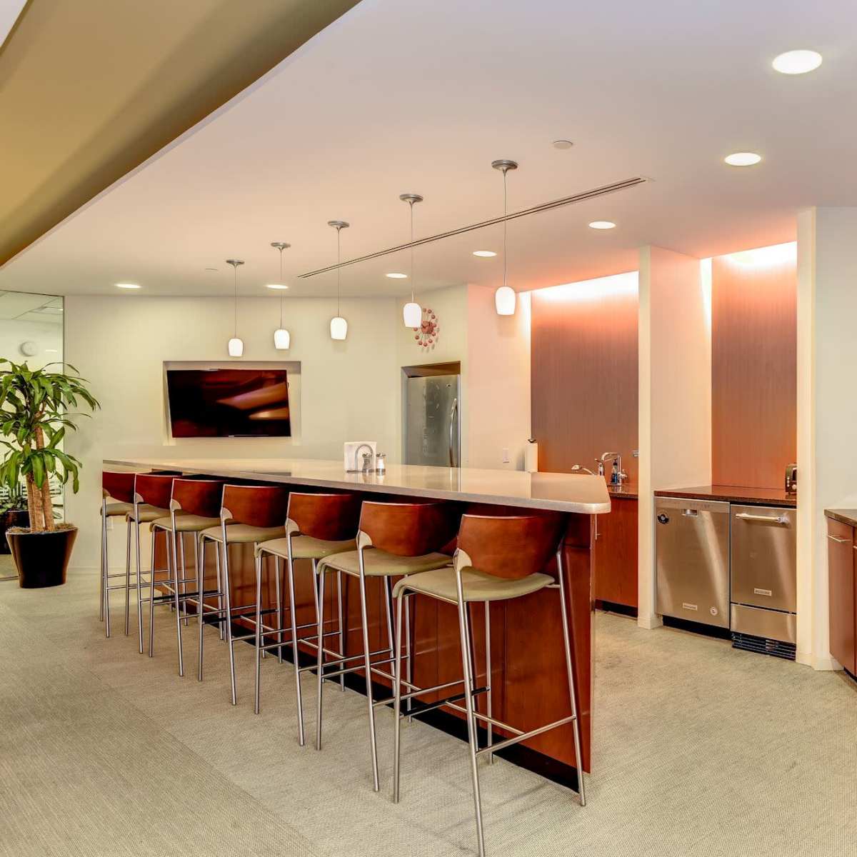 A modern kitchen bar area with high stools, a countertop, undercounter appliances, and a drink station.
