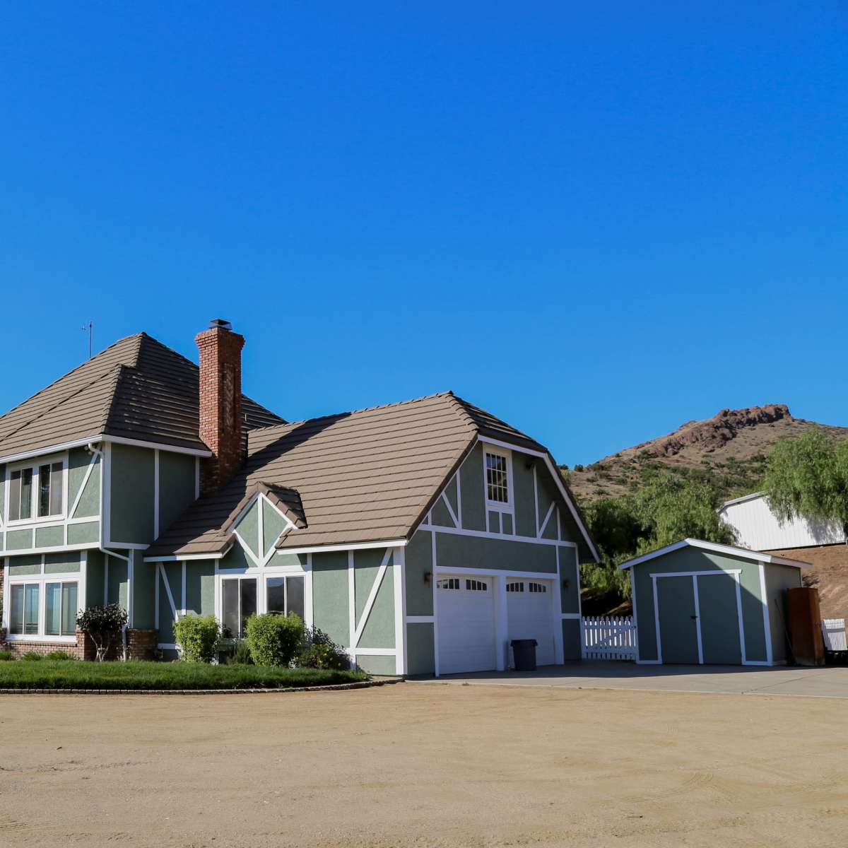 A large, two-story green house with a sloped roof, a brick chimney, and a well-maintained front lawn.