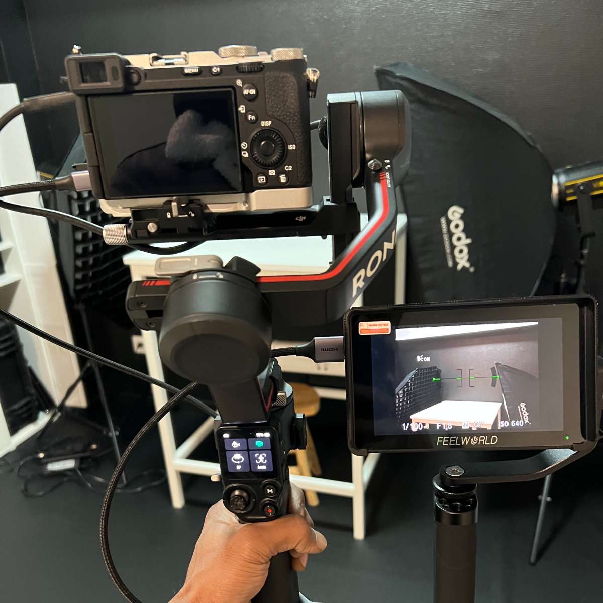 A person holds a camera mounted on a gimbal stabilizer with a monitor displaying a live feed attached.