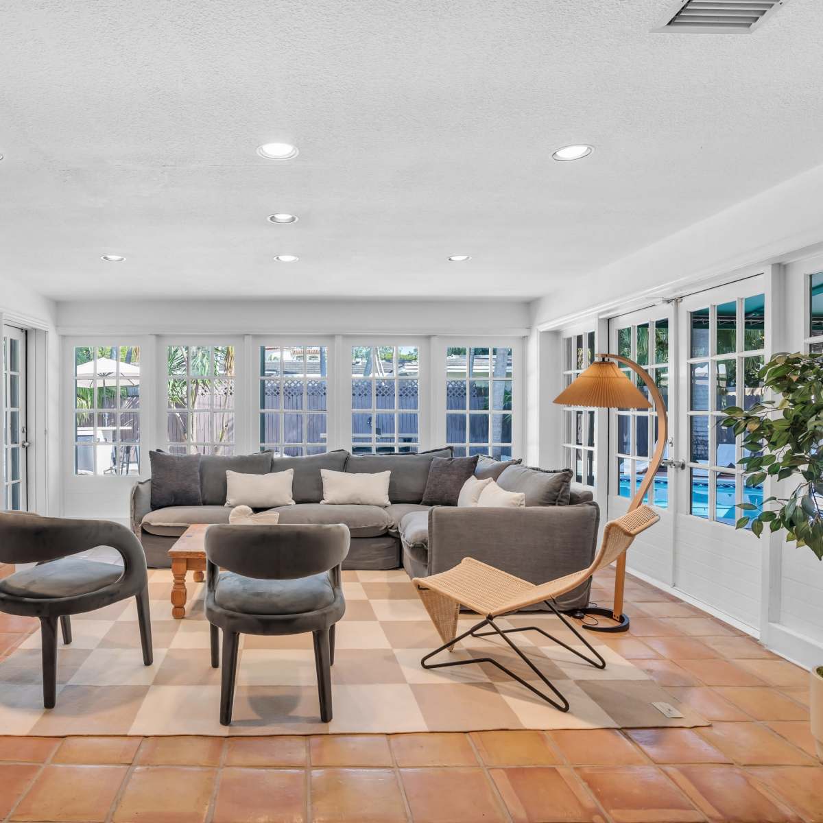 A bright living room with a sectional sofa, two armchairs, a wooden coffee table, and large windows overlooking a pool area.