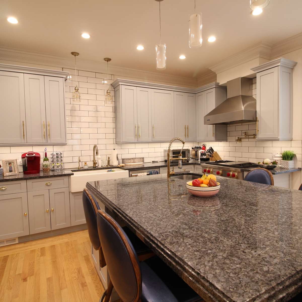A modern kitchen featuring gray cabinets, a large granite island, stainless steel appliances, and a white tile backsplash.