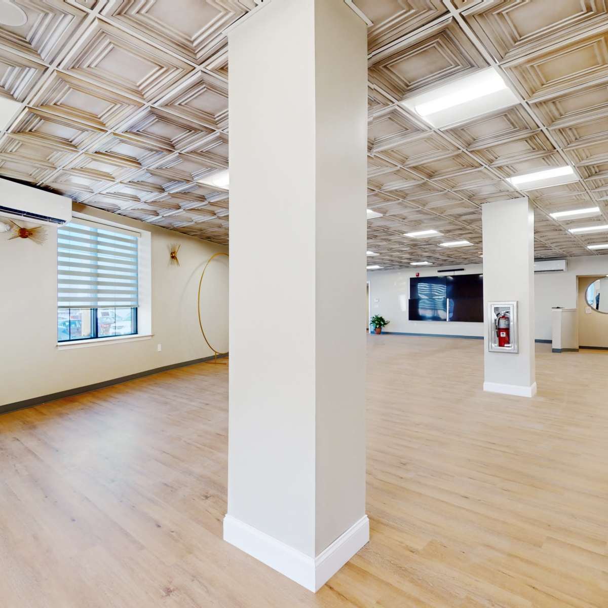 An empty interior space with wooden flooring, a textured ceiling, and large windows adorned with horizontal blinds.