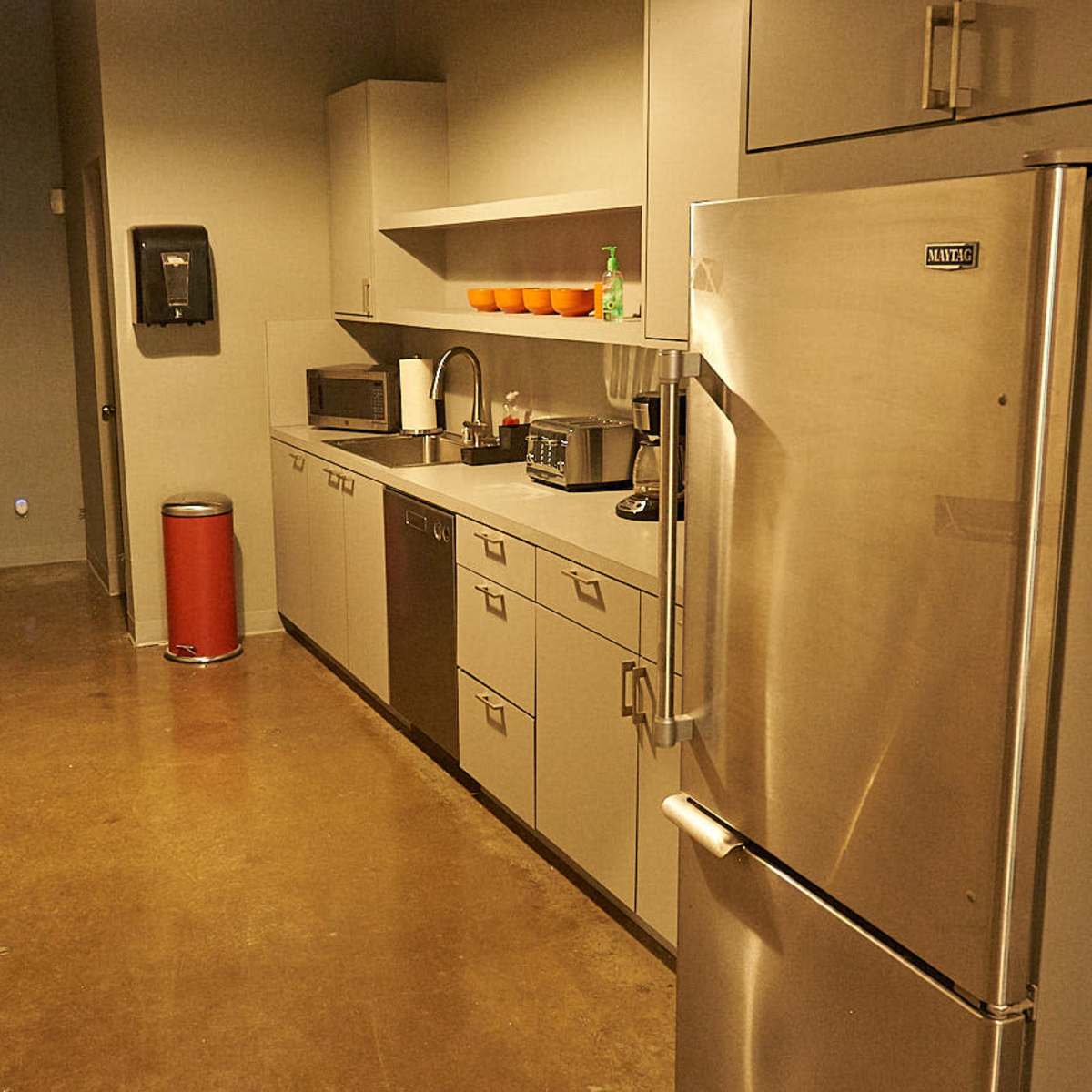 A narrow kitchen area with stainless steel appliances, gray cabinets, and a small table with two chairs.