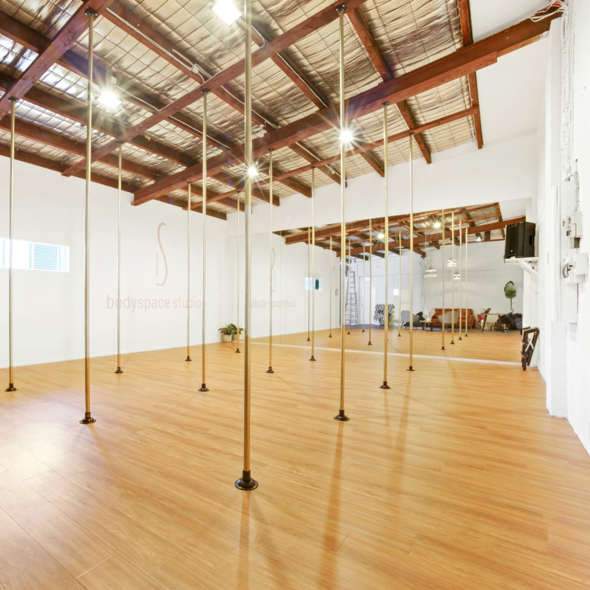 A spacious studio with wooden flooring, tall poles evenly spaced throughout, and a minimalist design featuring white walls and exposed wooden beams.