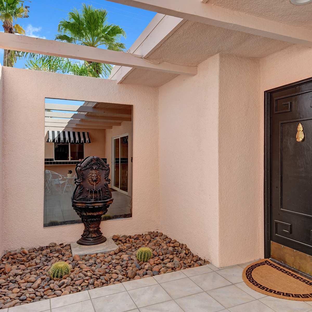 An entrance with a large black door, a decorative fountain in a landscaped area with pebbles, and a reflective mirror on the wall.