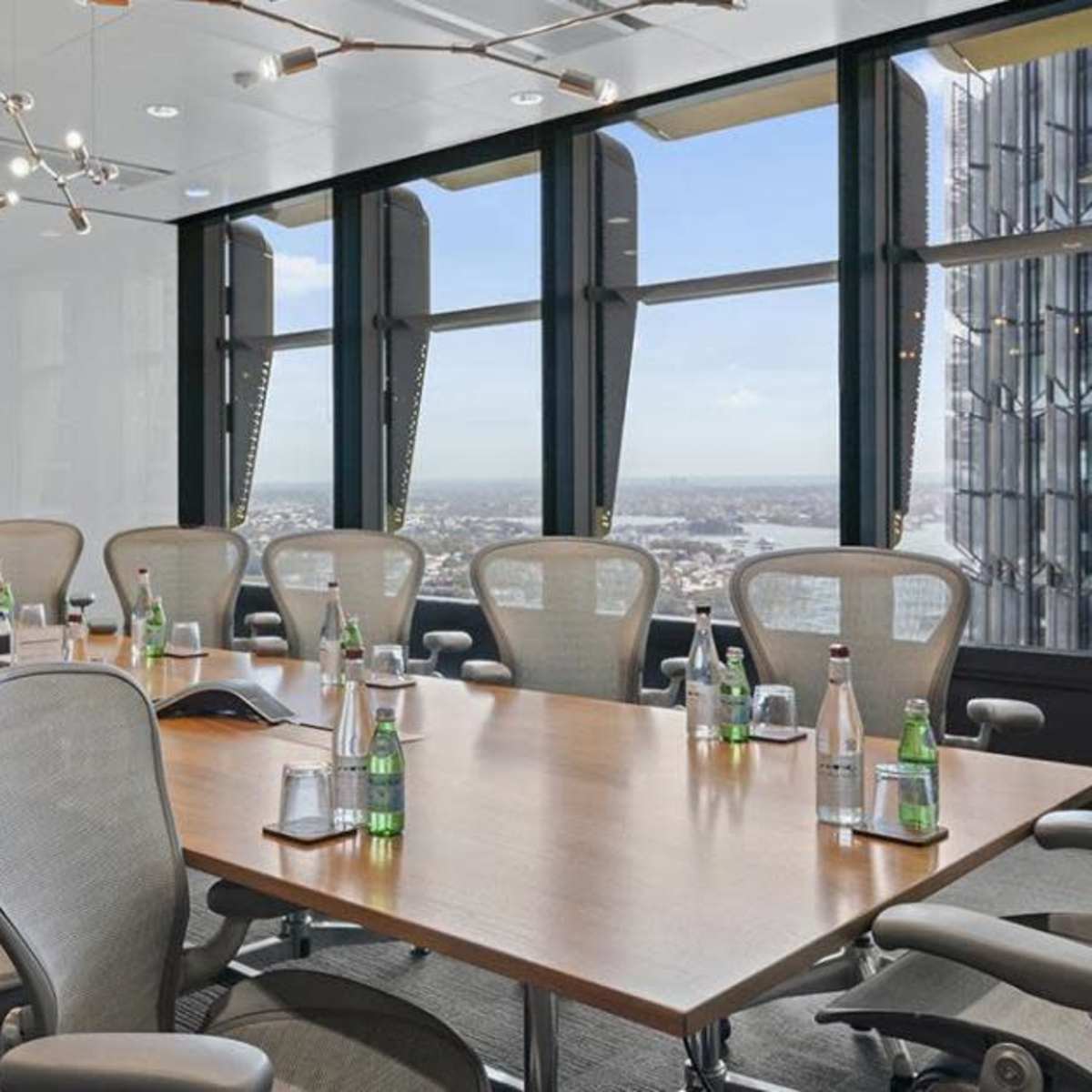 A modern executive conference room features a large wooden table surrounded by ergonomic chairs, with a screen displaying "The Executive Centre" and large windows offering a city view.