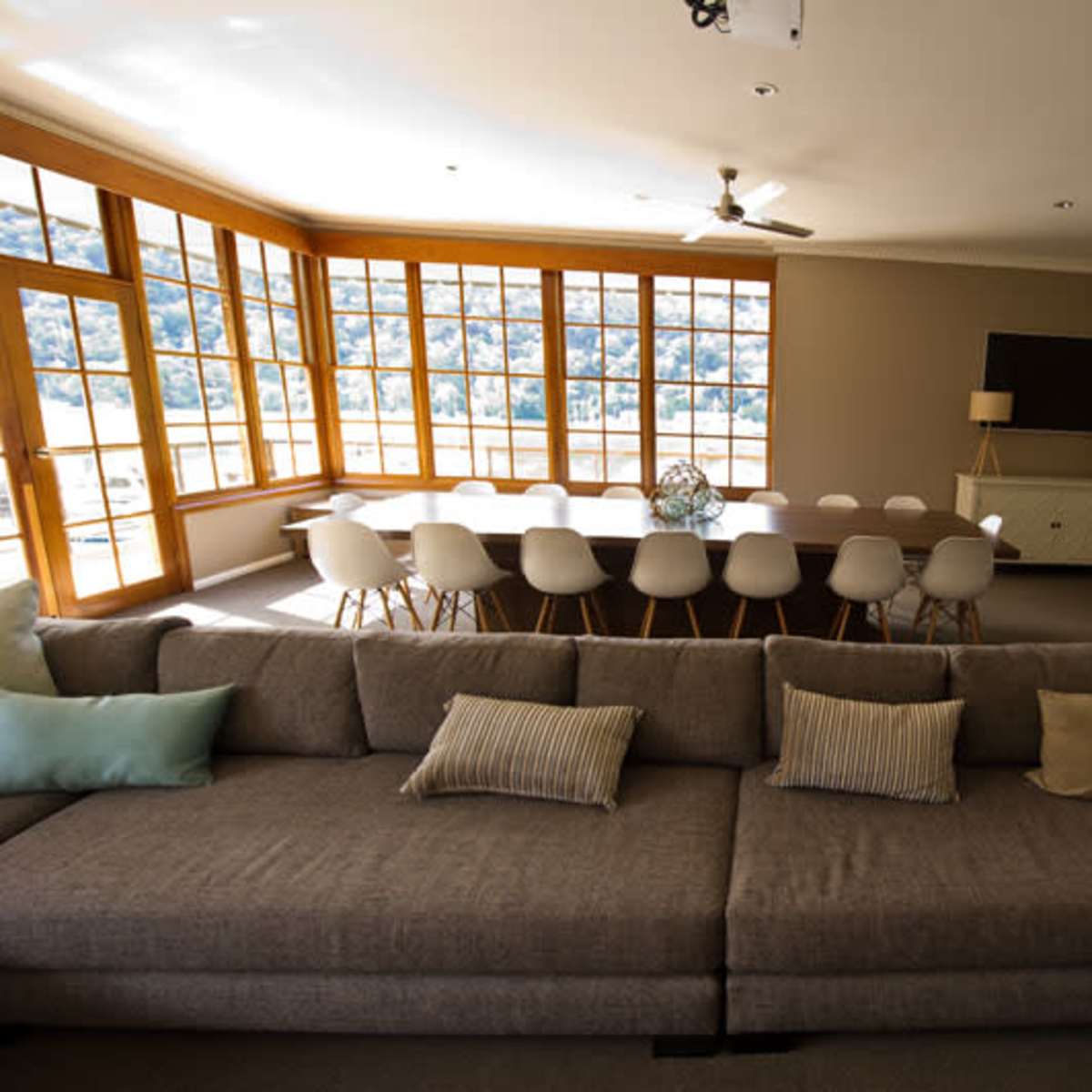 A spacious meeting room with a large table surrounded by chairs, large windows allowing natural light, and a comfortable couch with decorative pillows in the foreground.