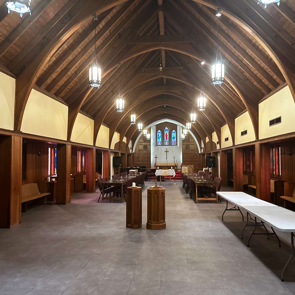 The interior of a church with a vaulted wooden ceiling, rows of seating on either side, and stained glass windows at the far end.