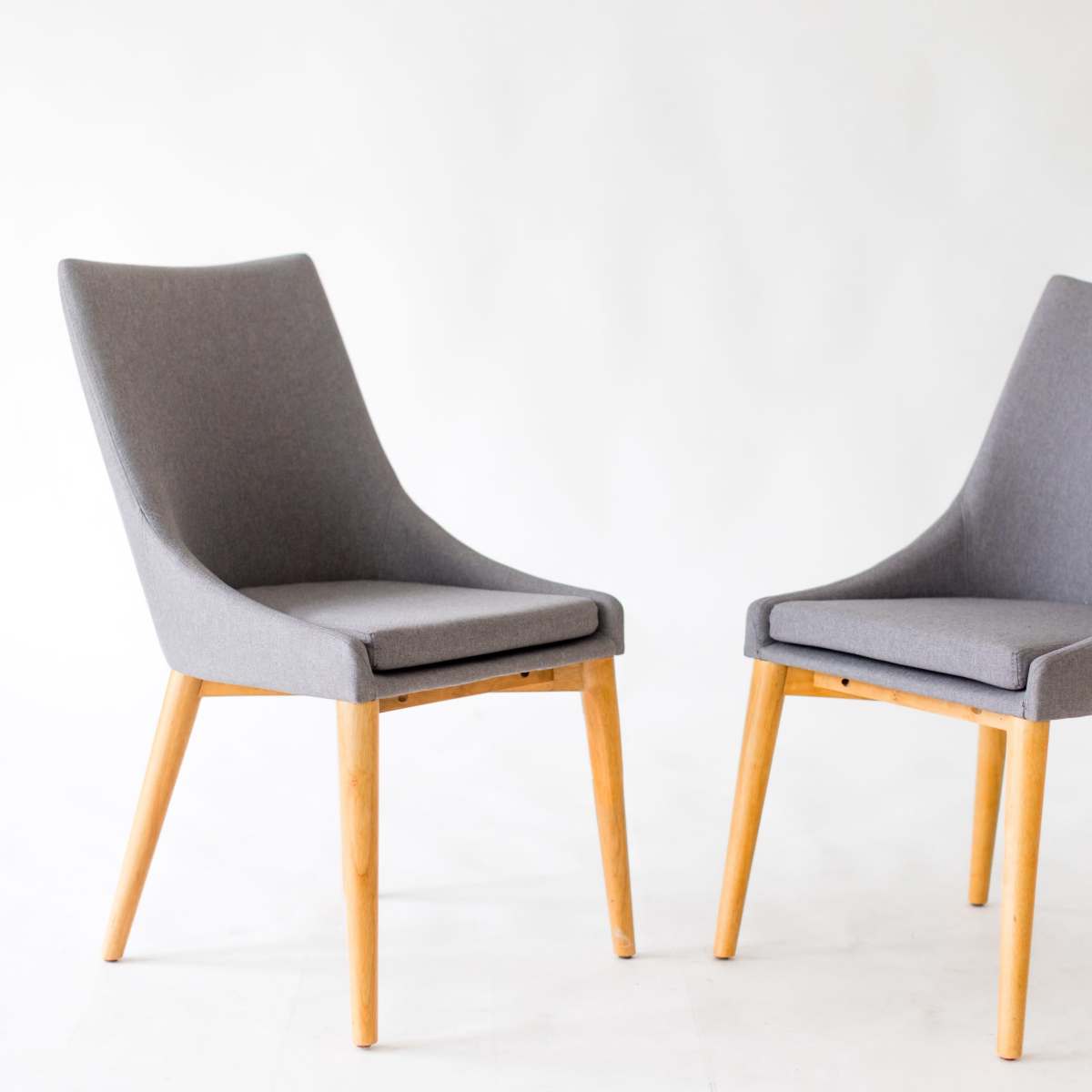 Two gray upholstered chairs with wooden legs are positioned facing each other on a plain background.