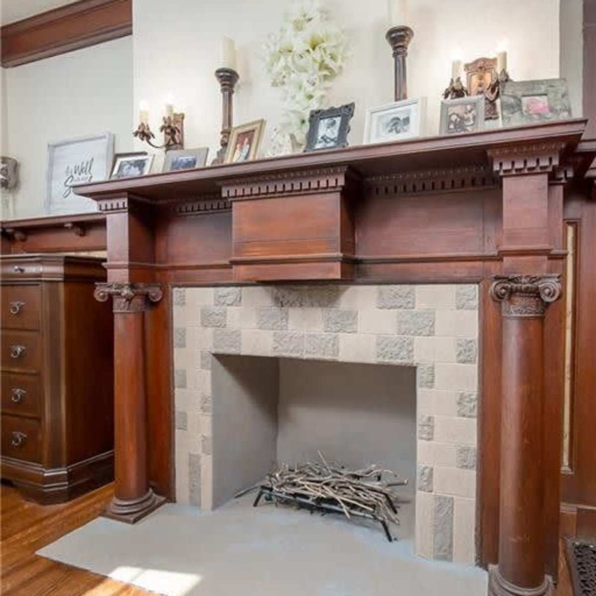 A wooden fireplace mantel with decorative photos and candles above a tiled firebox, complemented by a light gray hearth.