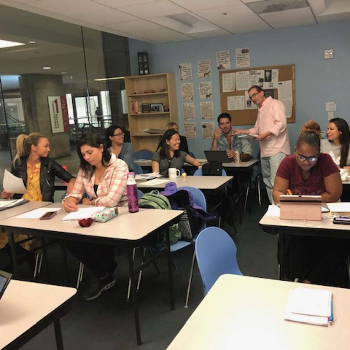 A group of students is engaged in discussion and studying at desks in a classroom setting.