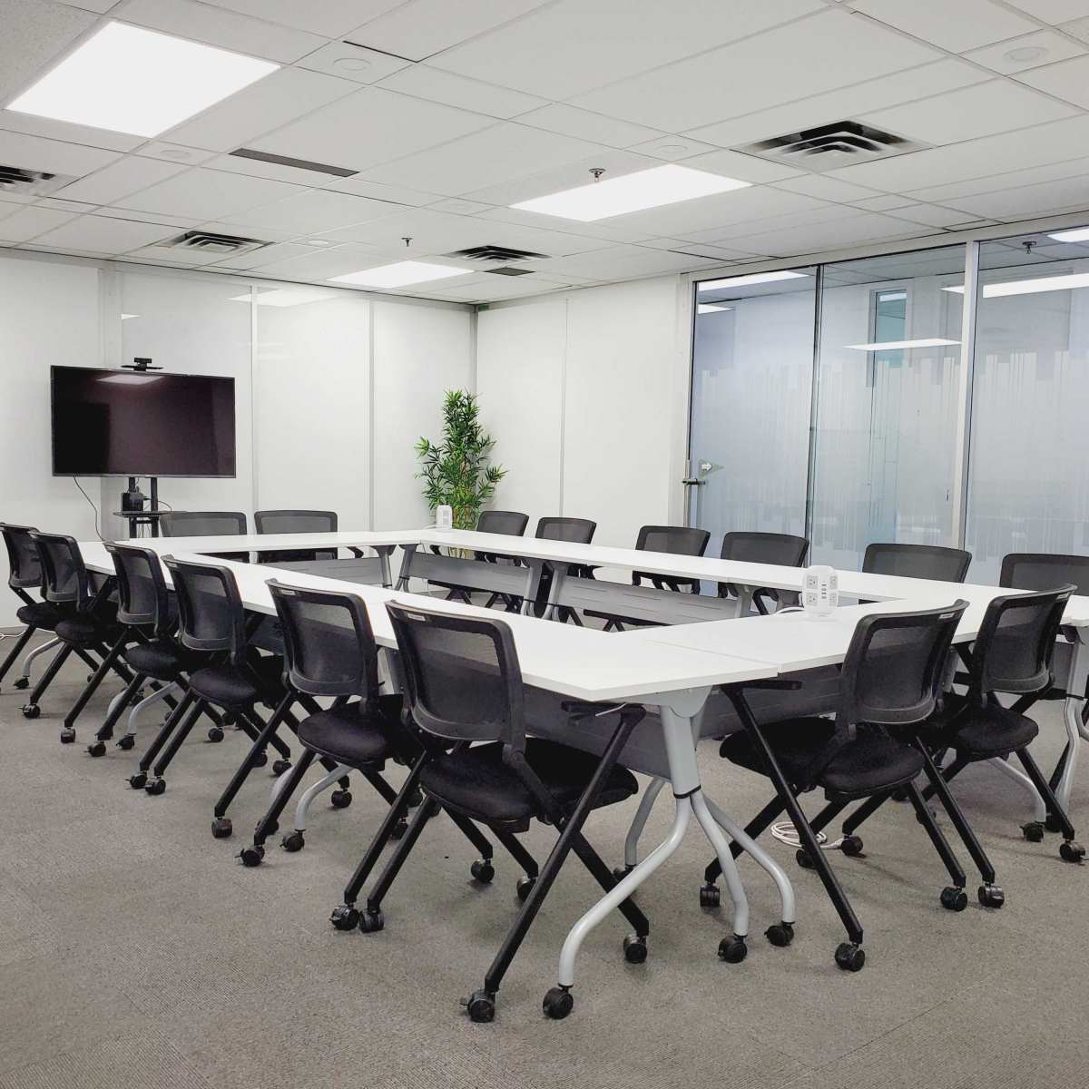 A modern conference room with a long white table, black chairs, a television display, and a whiteboard.