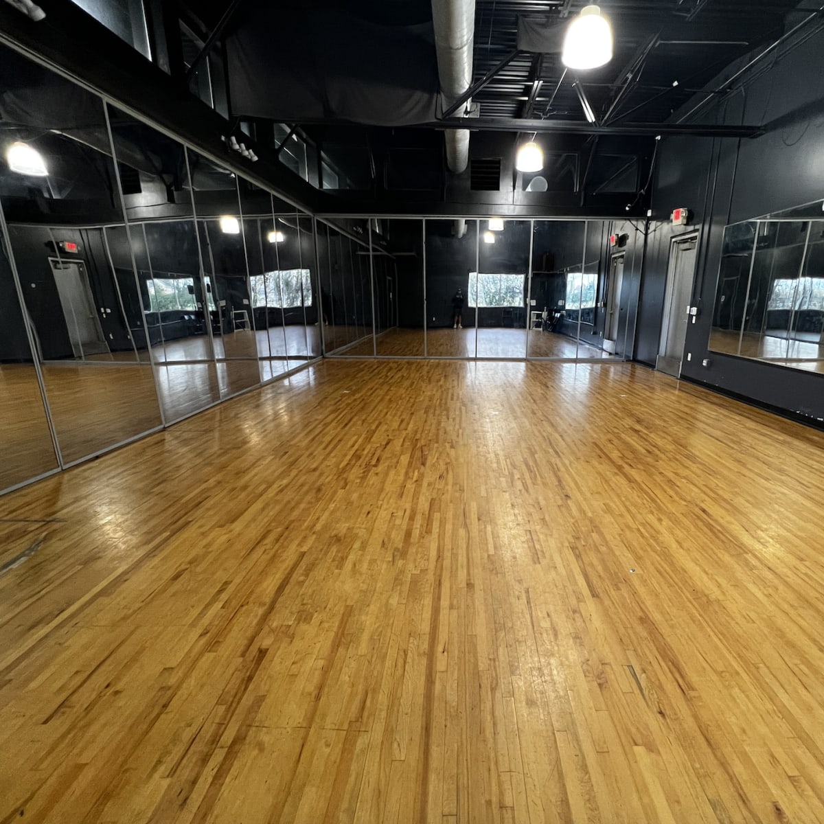 A large mirrored dance studio with polished wooden flooring and soft overhead lighting.