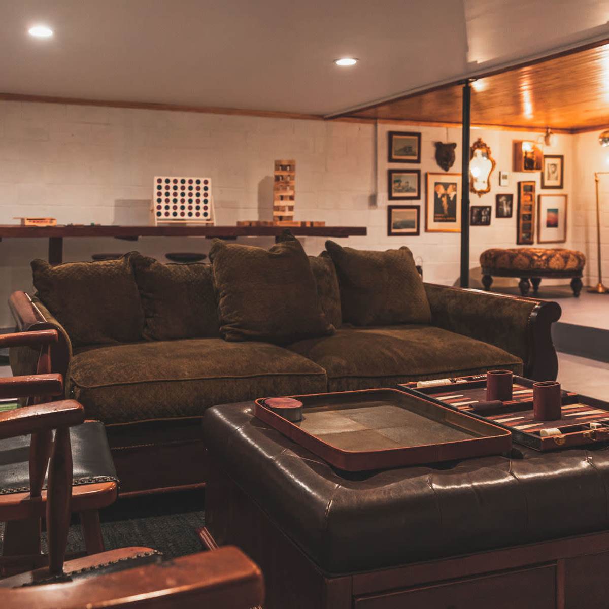 A cozy living room with a large brown sofa, wooden chairs, and a coffee table featuring a backgammon set, surrounded by framed pictures on the walls.