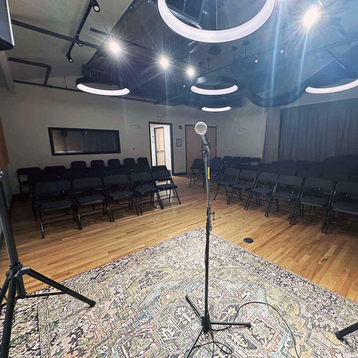A microphone stands on a stand in front of a row of empty chairs arranged for an event in a well-lit room.