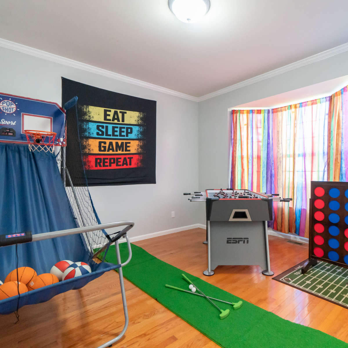 The room features a basketball shooting game, a foosball table, a large Connect Four game, and decorative walls with colorful curtains and sports-themed banners.