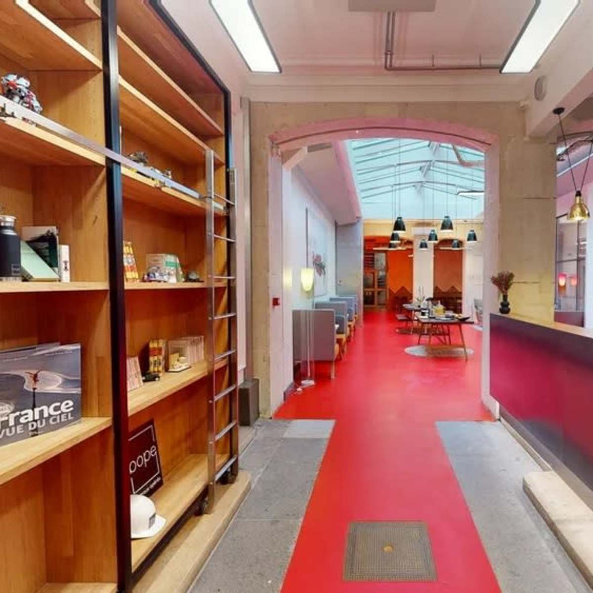 A modern interior with a red carpet, a wooden reception desk on the right, and shelves displaying various items along the left wall.