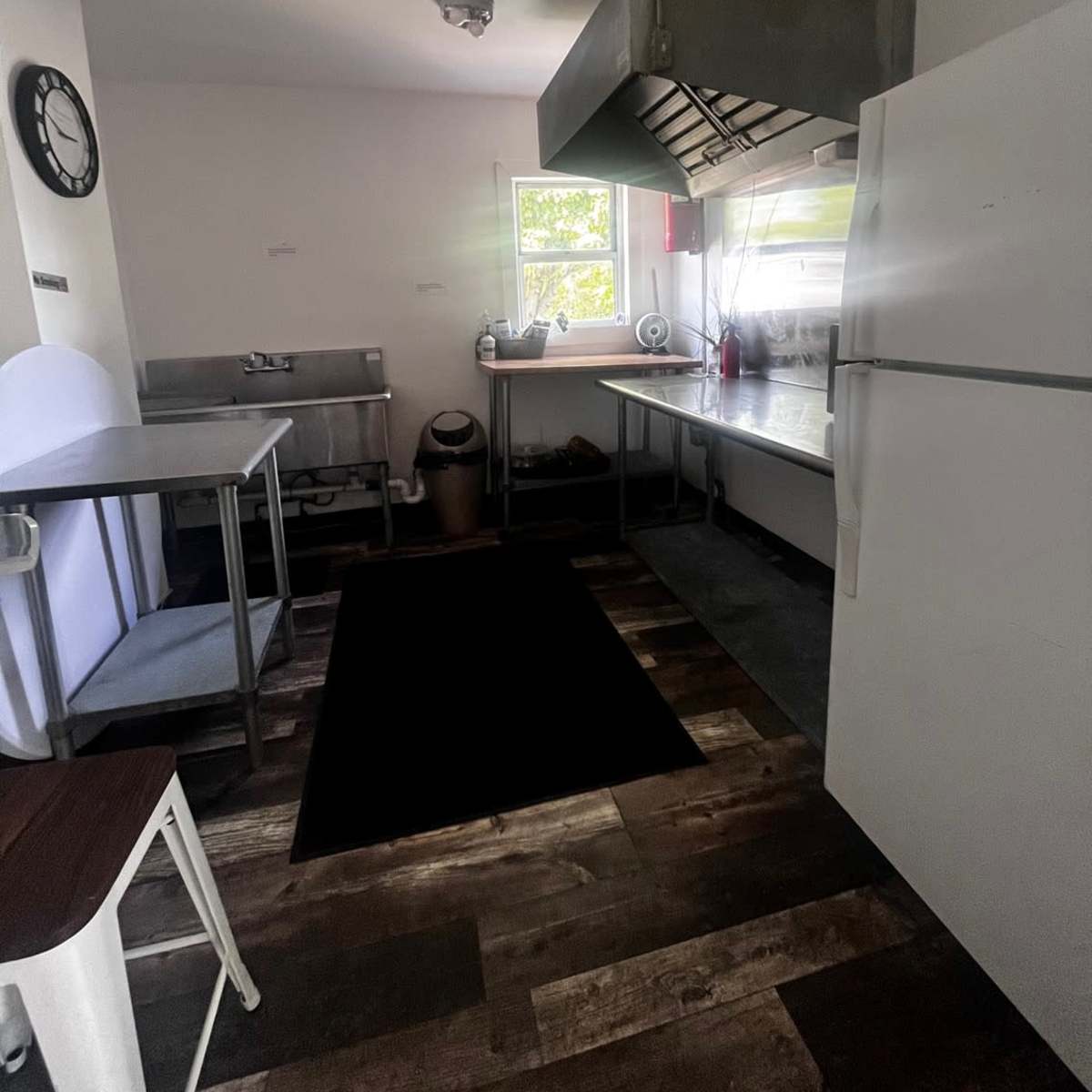 A kitchen with metal countertops, a large range hood, a white refrigerator, and a window allowing natural light.