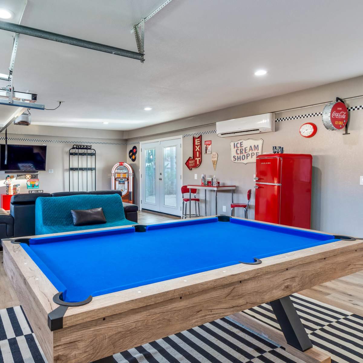 A recreational room featuring a blue pool table, teal seating, a vintage-style ice cream shop-themed refrigerator, and various decor elements.