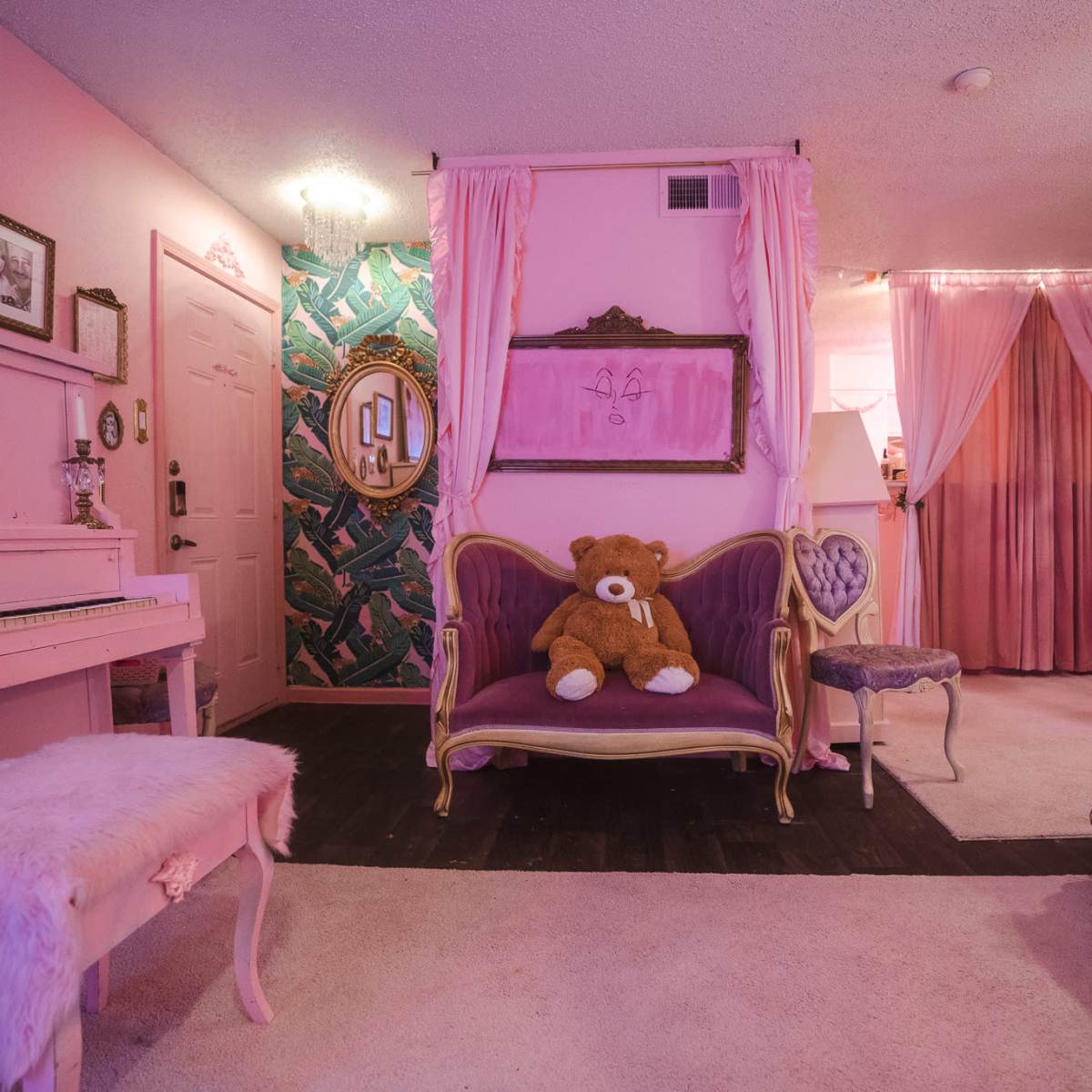 The room features pink walls, a vintage piano, a plush sofa with a teddy bear, and ornate furniture.